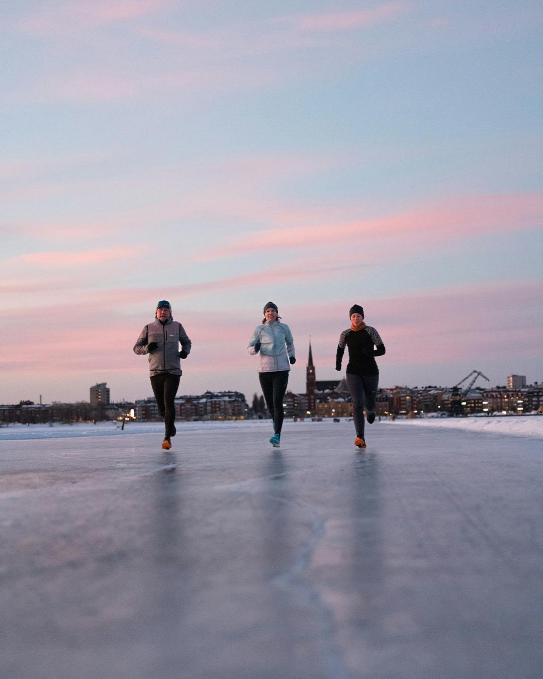 three people running on the ice with a city in the background