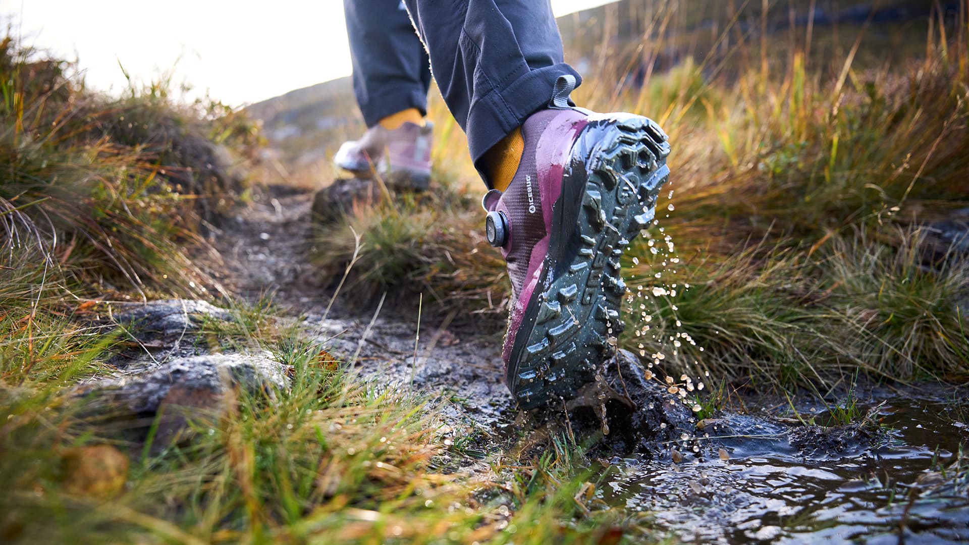 A person walks through a stream in hiking shoes from Icebug, splashing water and embracing the outdoors.