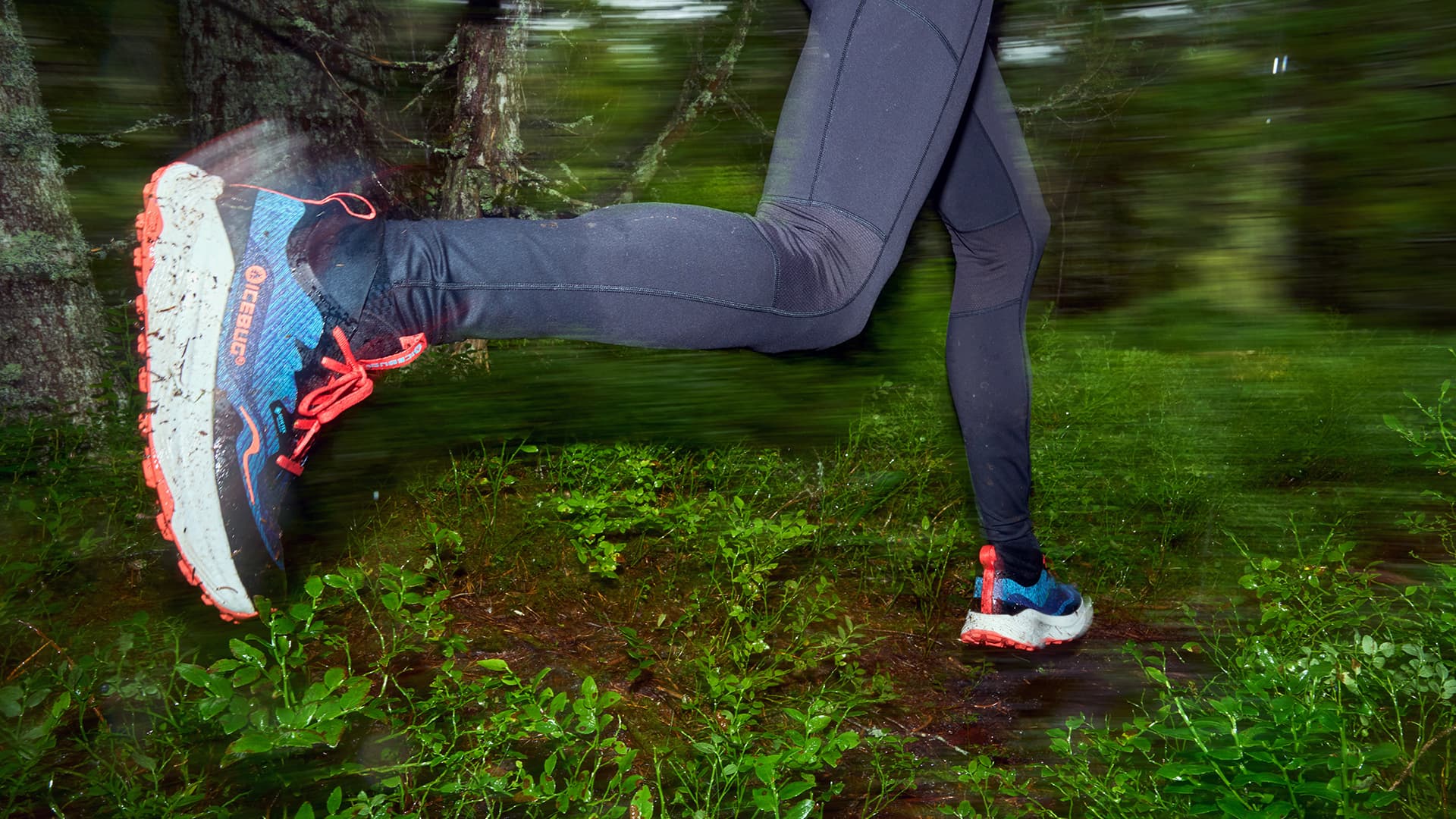 Person running through a forest in black leggings and colorful Icebug trail running shoes, with blurred background indicating motion.