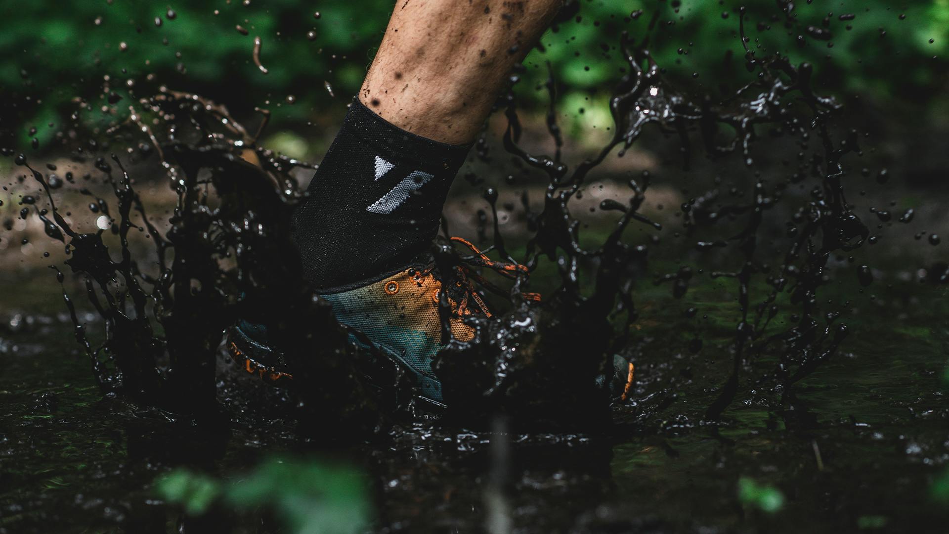 A person running in mud with a pair of Icebug Acceleritas Trail Running Shoes