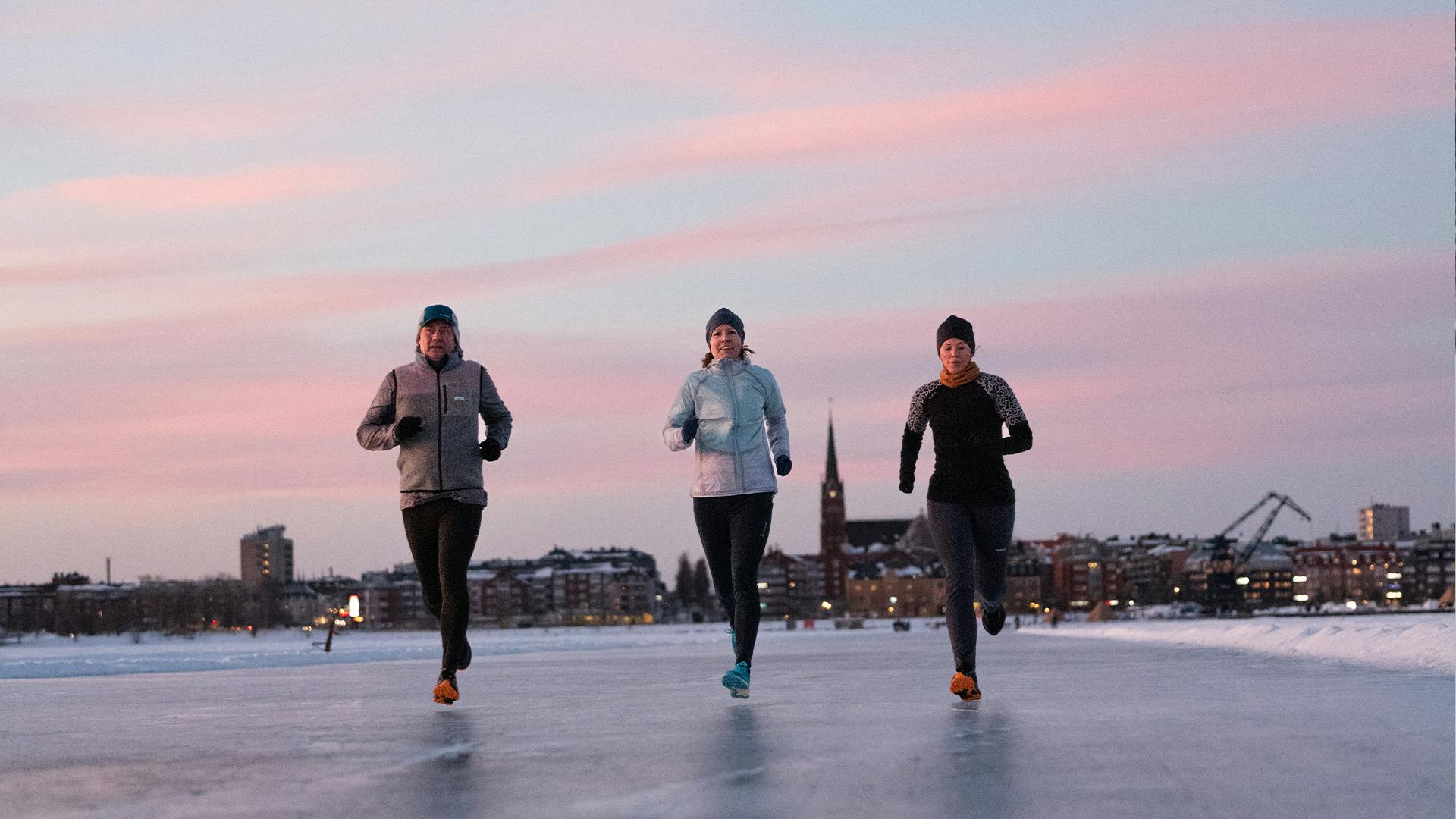 three people running on the ice with a city in the background