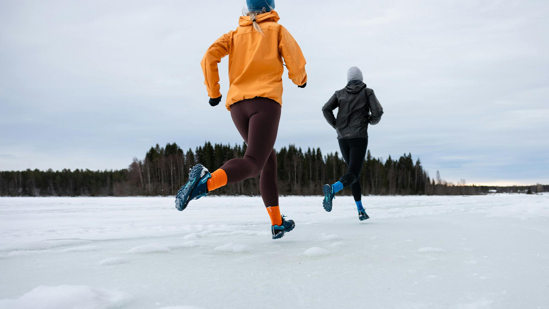 Two people are running on snow and ice with Icebug Pytho6 BUGrip on their feet.